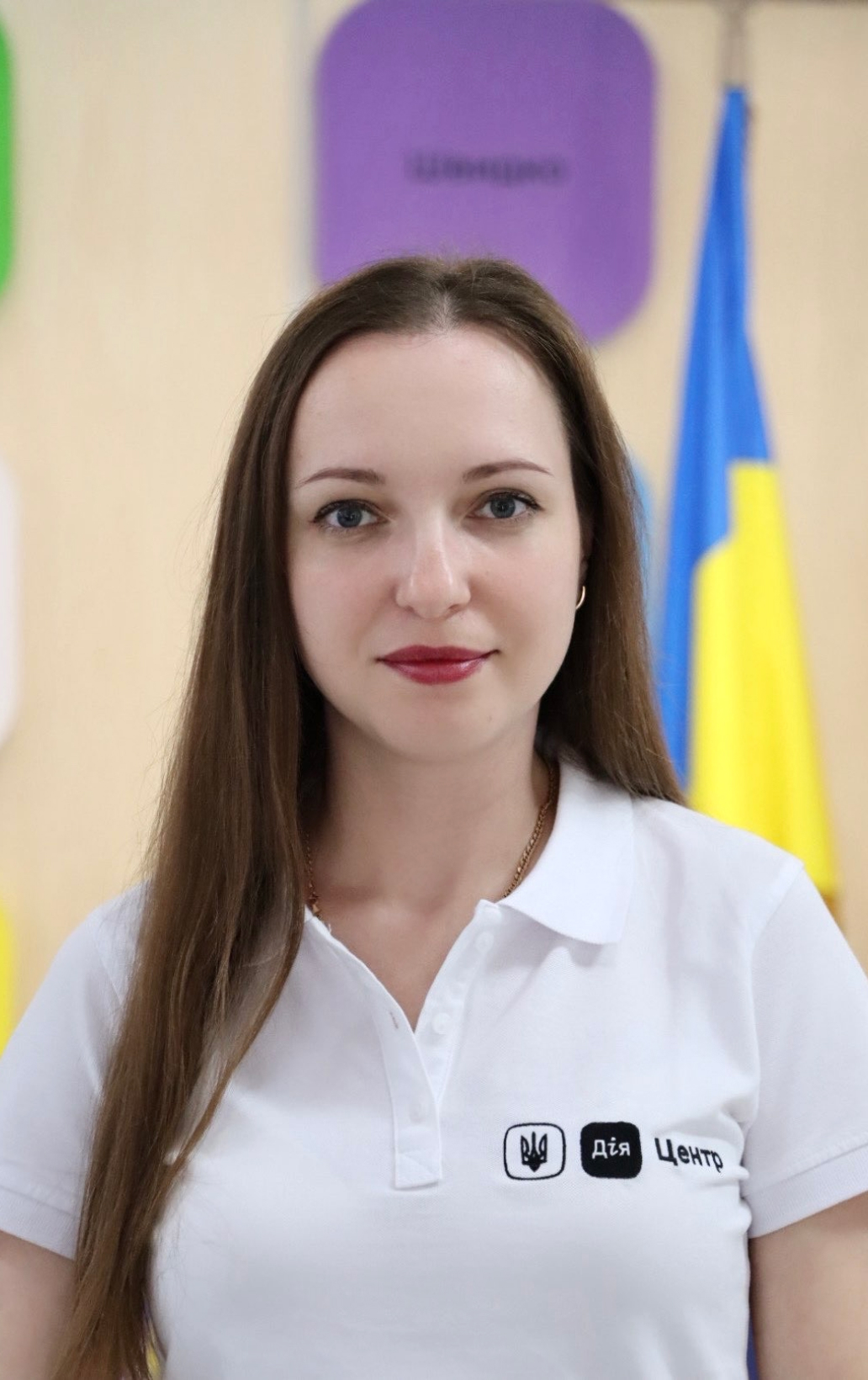 Жінка з довгим русявим волоссям, у білій футболці з логотипом.